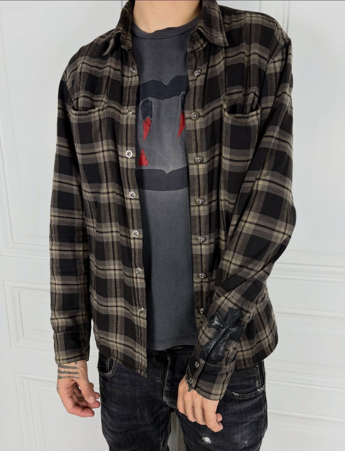 Person wearing a black and tan plaid flannel shirt over a dark graphic t-shirt and jeans.