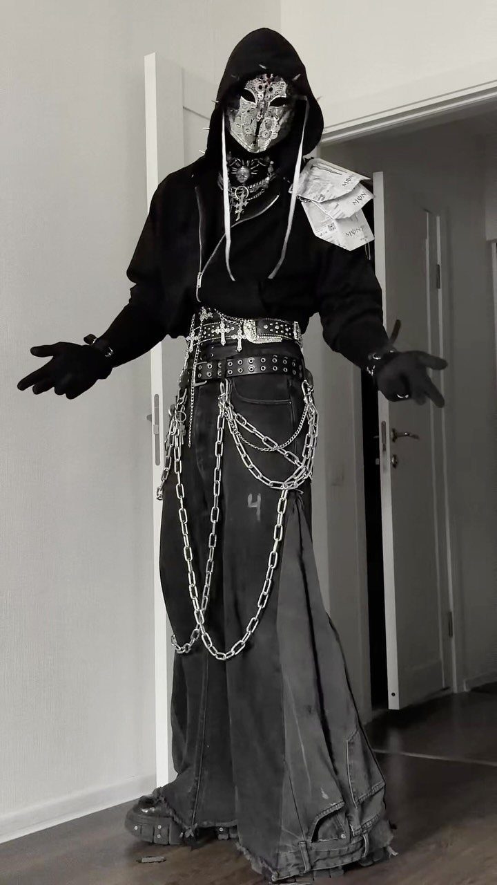 Person in black alternative fashion wearing a mask, hoodie, and wide trousers with silver chains.