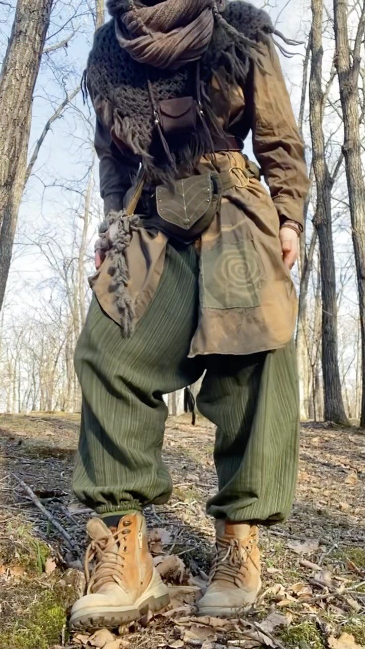 Person in earth-toned layered clothing and hiking boots standing in a forest.