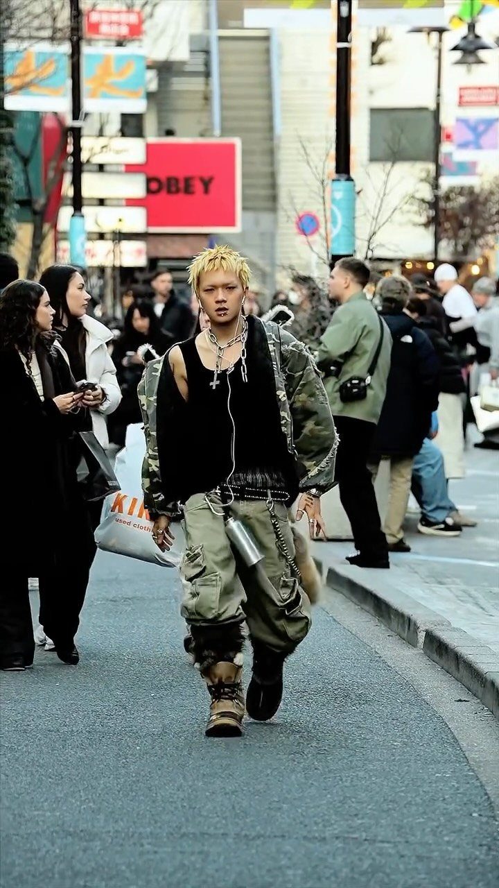 A young man with blonde hair walks through a city street wearing alternative streetwear fashion.