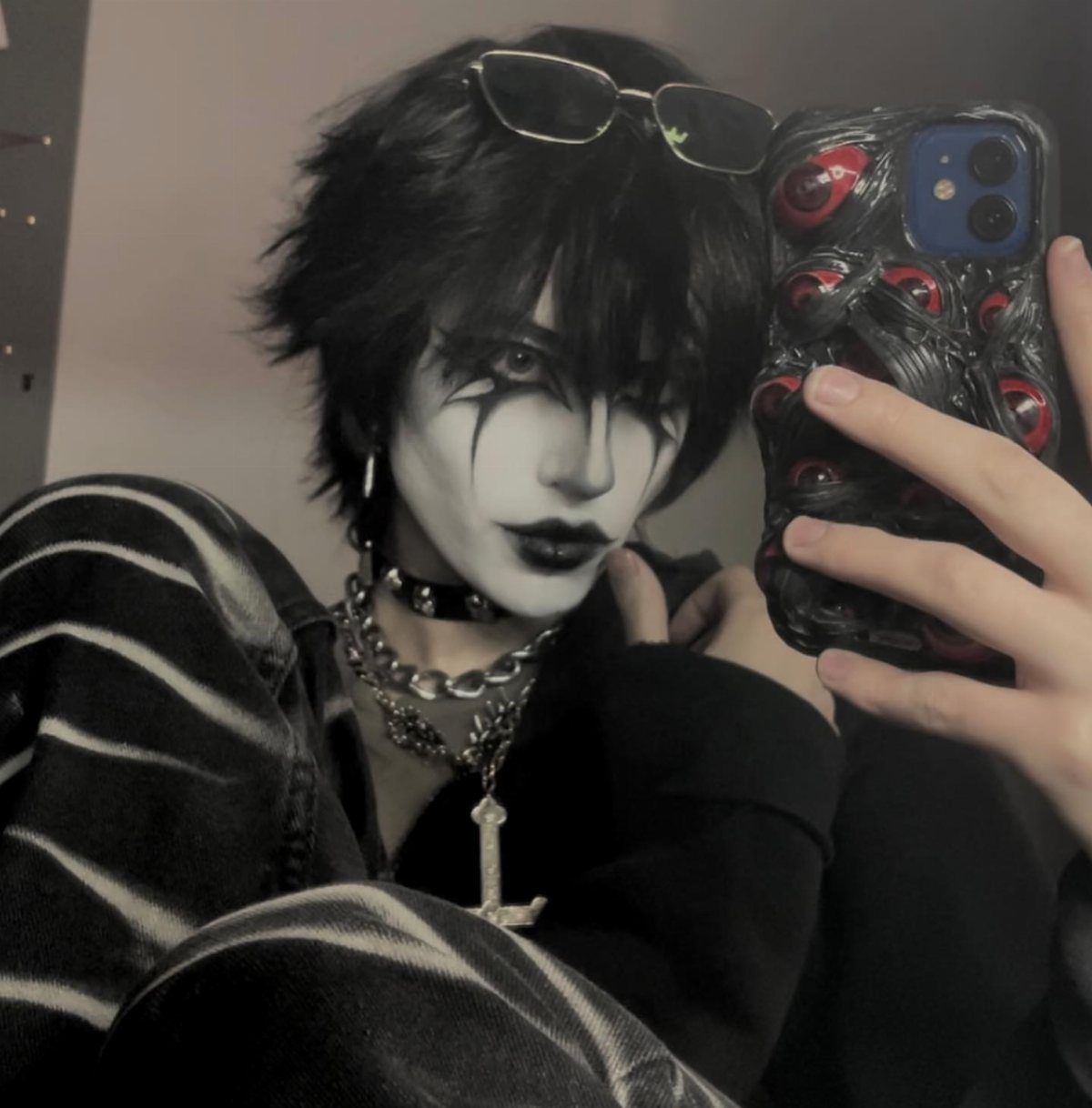 Person with dramatic black eye makeup and silver chains posing for a mirror selfie.