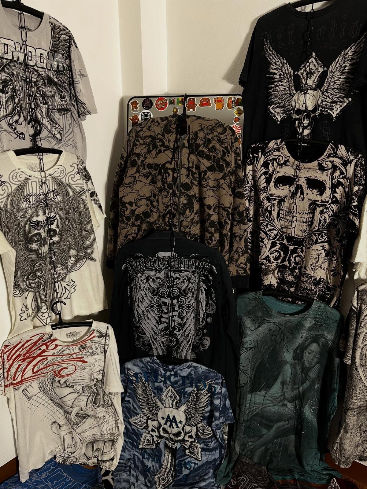 Graphic t-shirts with skull and wing designs hanging on a wall in a dark aesthetic style.