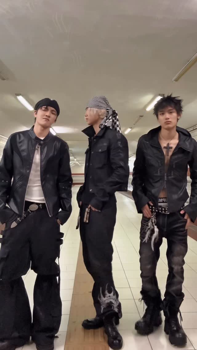 Three young men posing in dark streetwear and leather jackets in a subway station.