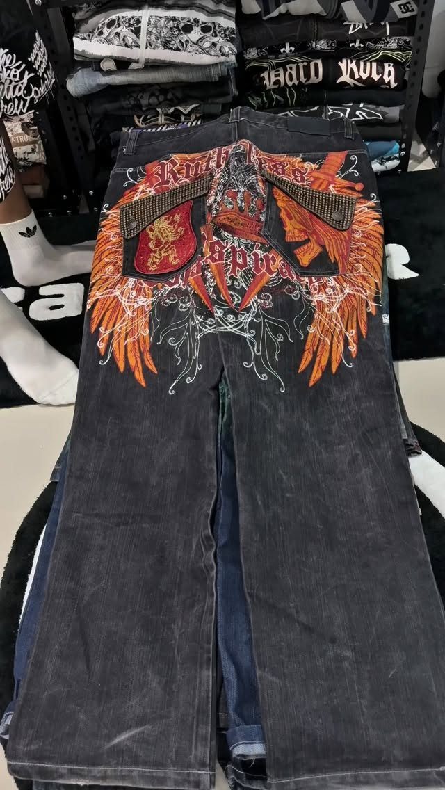 Dark denim jeans with large orange wing embroidery and red text on the back.