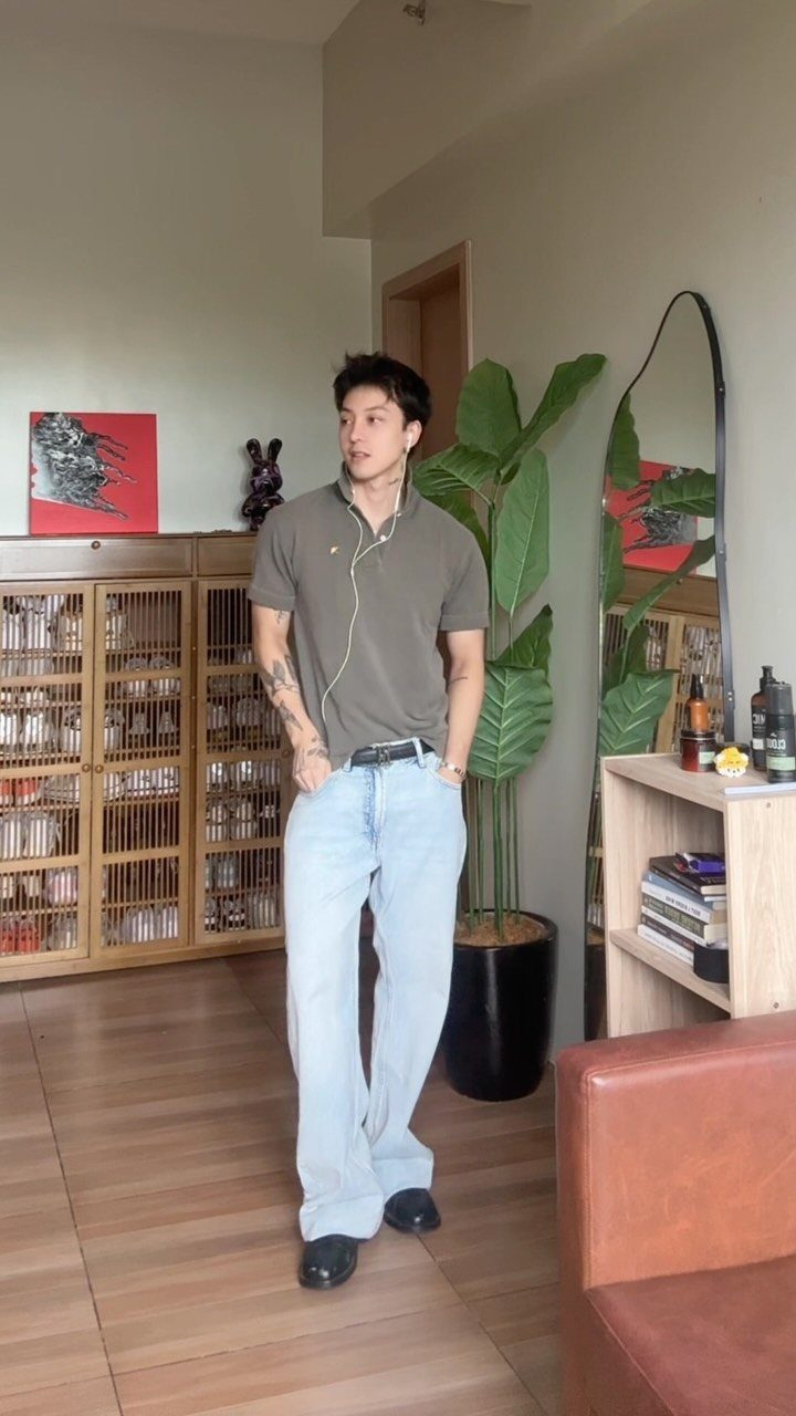 A man posing in an olive polo shirt and baggy light blue jeans.