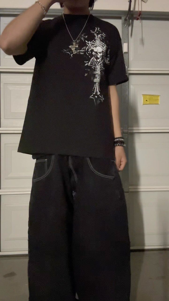 Person wearing an oversized black graphic t-shirt and baggy black pants with white stitching.