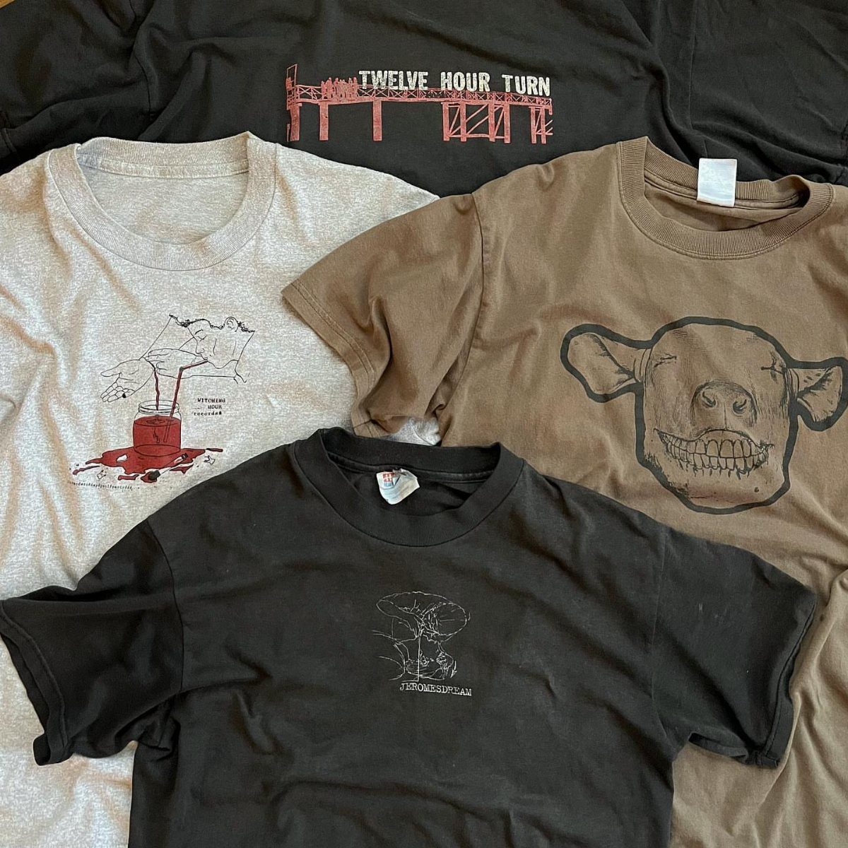 Four graphic t-shirts in black, grey, and brown laid flat on a surface.