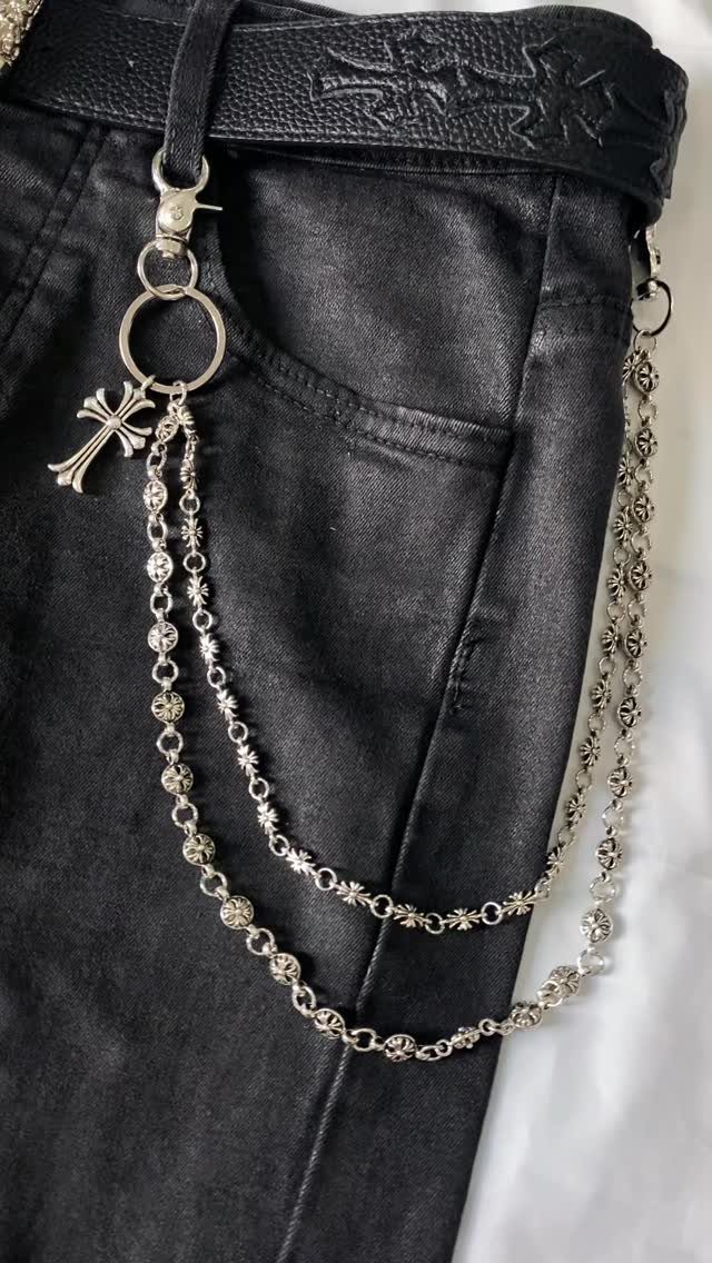 Silver metal pant chains with cross charms hanging from black denim jeans.