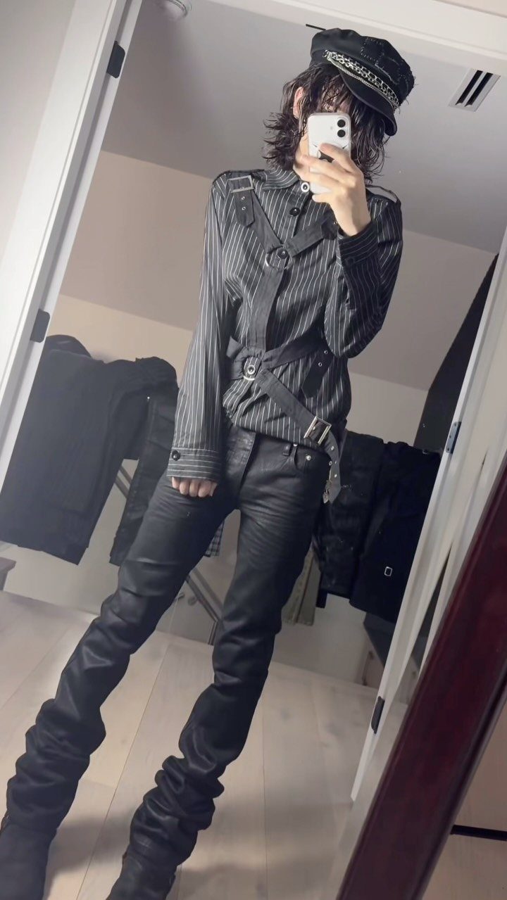 Person wearing a pinstriped jacket, black skinny jeans, and a military cap posing for a mirror selfie.