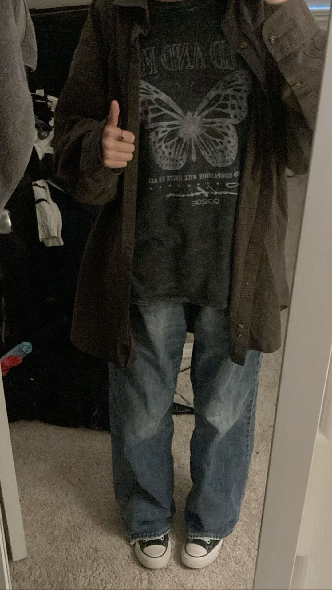 A person wearing a baggy butterfly graphic t-shirt, oversized dark shirt, and loose denim jeans.