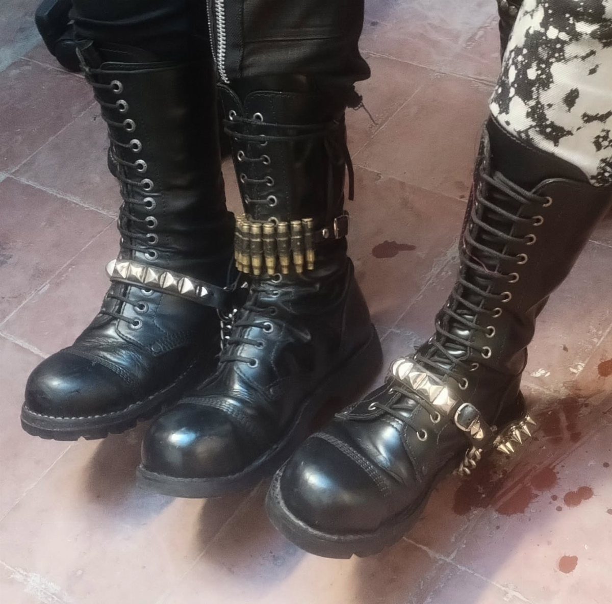 Three pairs of black leather combat boots with silver studs and metal decorations on a floor.