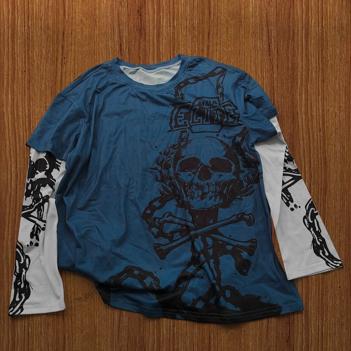 A blue and white long-sleeved t-shirt with a black skull and crossbones graphic on a wooden background.