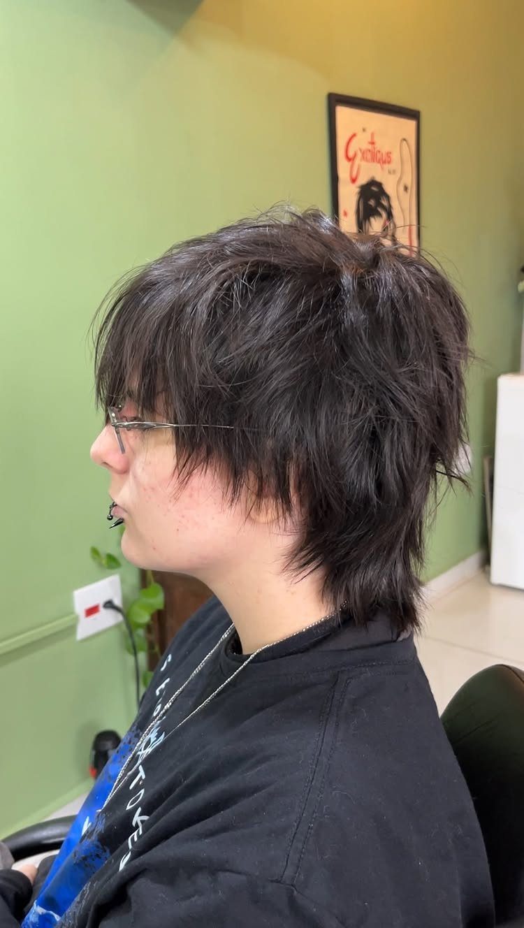 A person with dark, voluminous, shaggy layered hair shown in profile against a green wall.