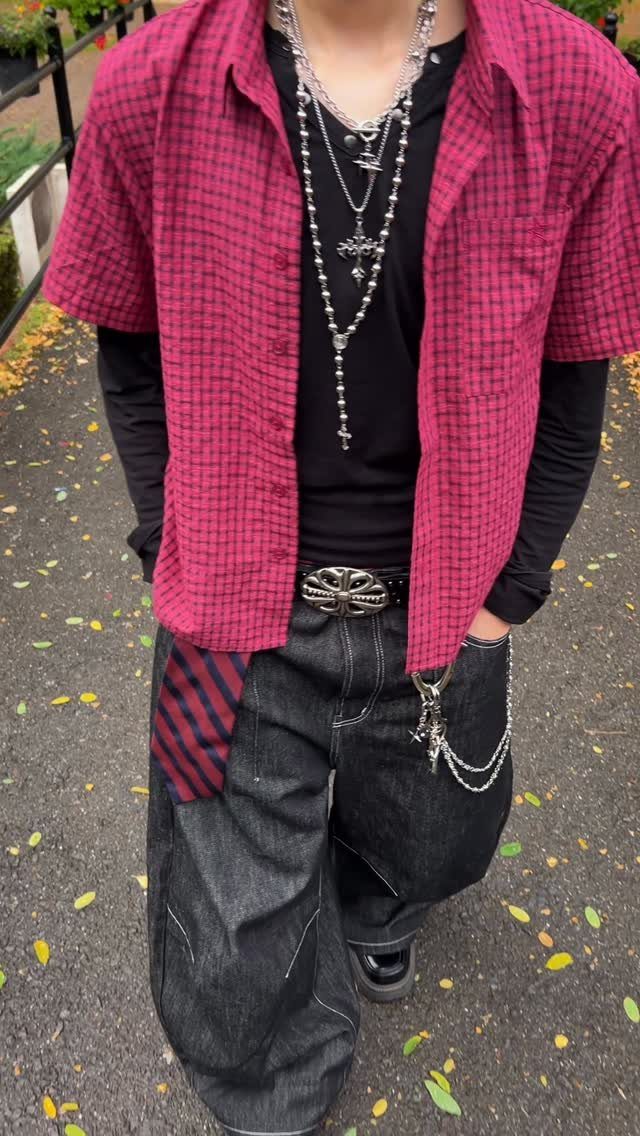 Person wearing layered clothing including a pink checkered shirt over a black long-sleeve shirt and necklaces.