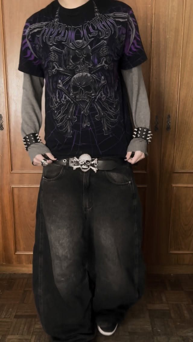 Person wearing a black skull graphic t-shirt, baggy black jeans, and studded wristbands.