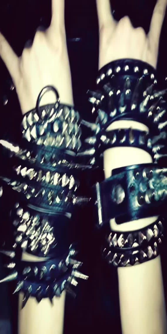 Two arms wearing multiple thick black leather wristbands with long silver metal spikes and studs.