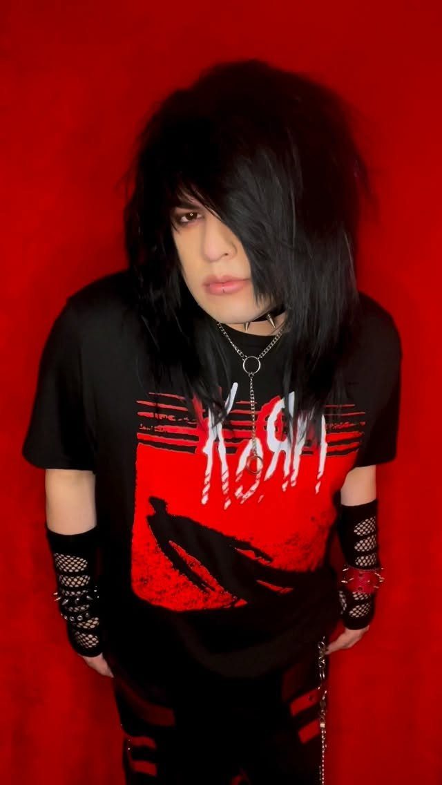 Person with black hair wearing a black Korn band t-shirt against a red background.