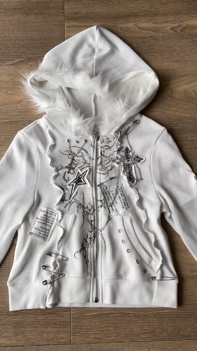 White hooded sweatshirt decorated with safety pins, star patches, and black scribbled line art.