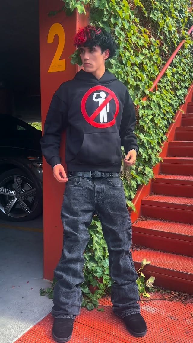 Young man with red and black hair posing in a black hoodie and dark grey jeans.