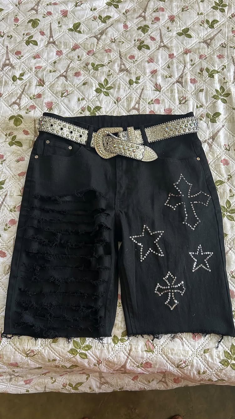 Black distressed denim shorts with silver rhinestone stars and crosses on a floral bedspread.