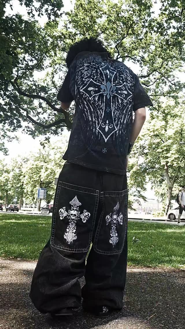 Person wearing an oversized black graphic t-shirt with a large white cross design and wide black pants.