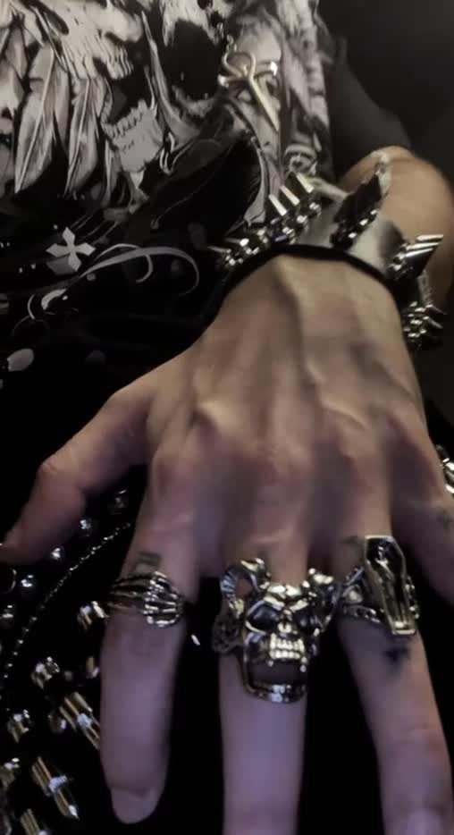 A hand wearing large silver skull rings and a black studded leather wristband.