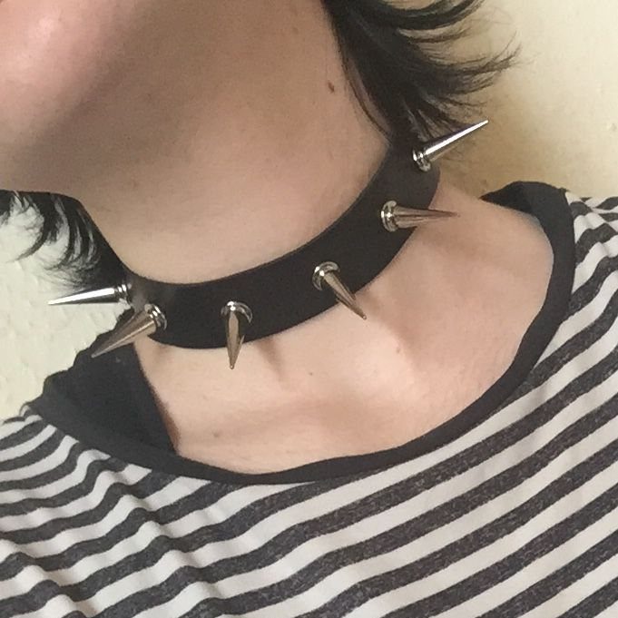 A person wearing a black leather choker with long silver metal spikes around their neck.
