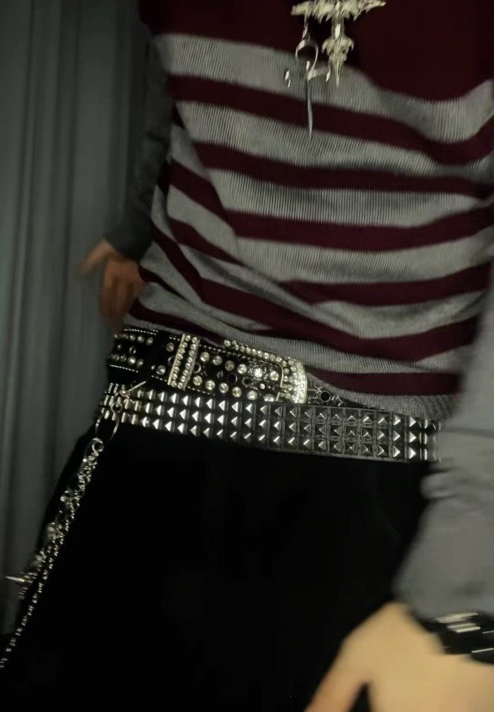 Person wearing two wide black belts decorated with silver metal studs over black pants.