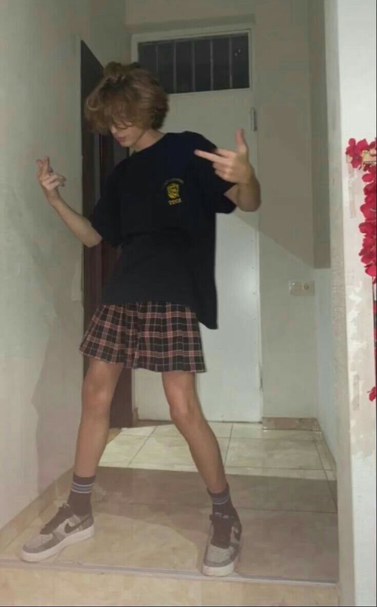 A person posing in a black graphic t-shirt and a plaid mini skirt.