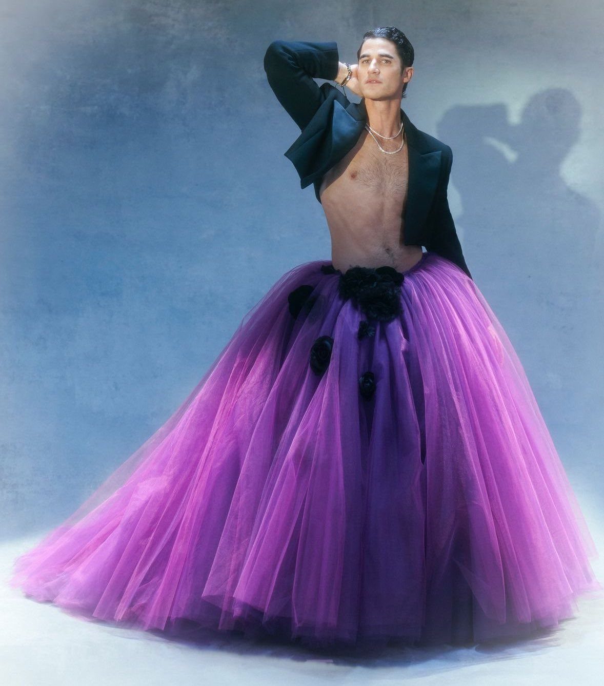 A person posing in a large, high-waisted purple tulle skirt and a black cropped jacket.