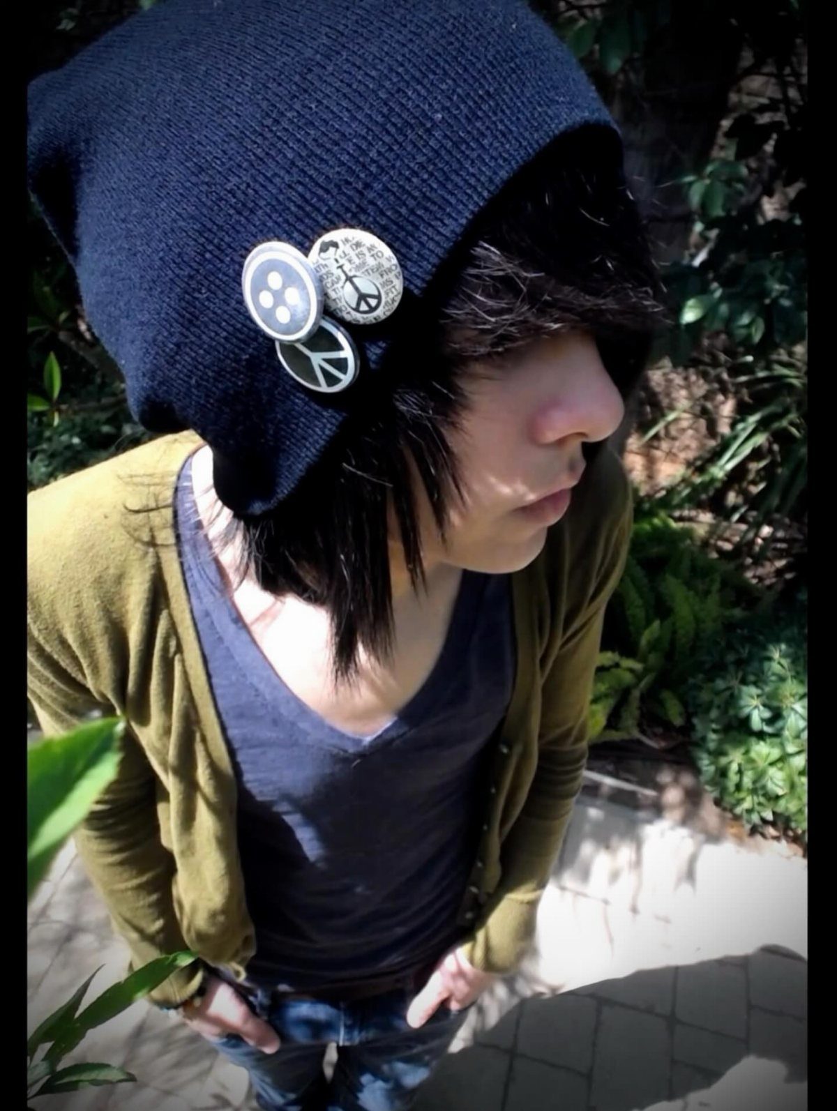 A person wearing a navy blue beanie with decorative pins and an olive cardigan.