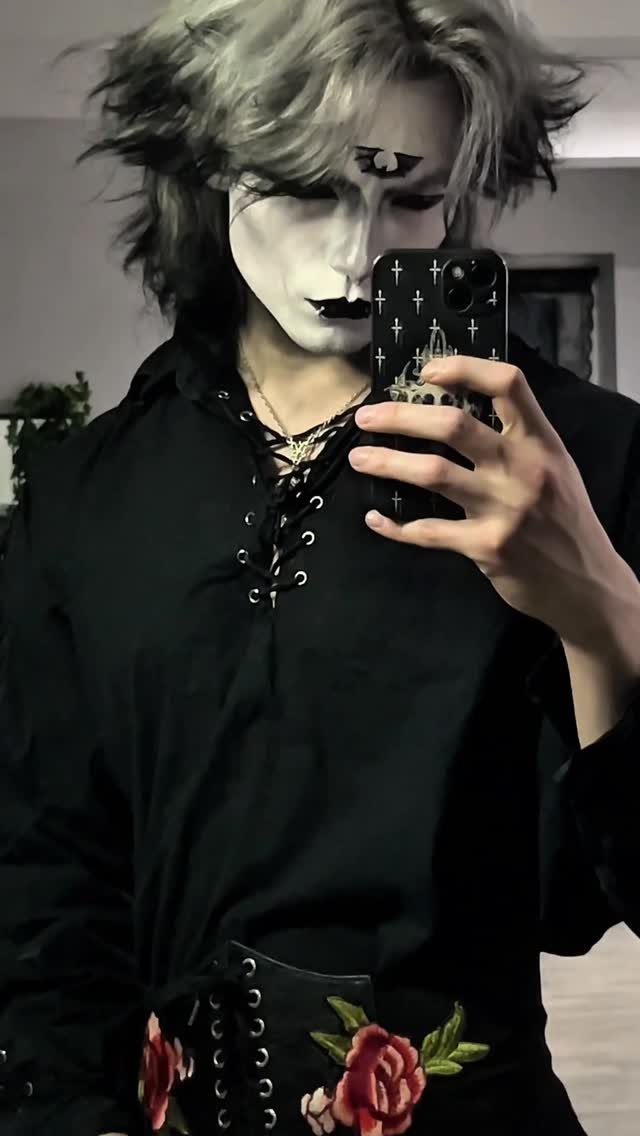 Person with white face paint and dark eye makeup taking a mirror selfie.