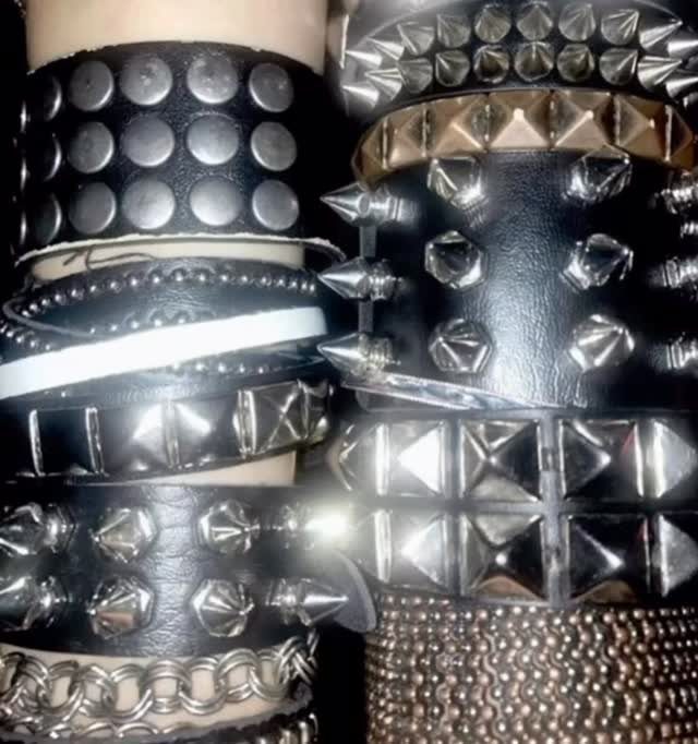 Multiple black leather bracelets with silver metal studs, spikes, and chains worn on a wrist.