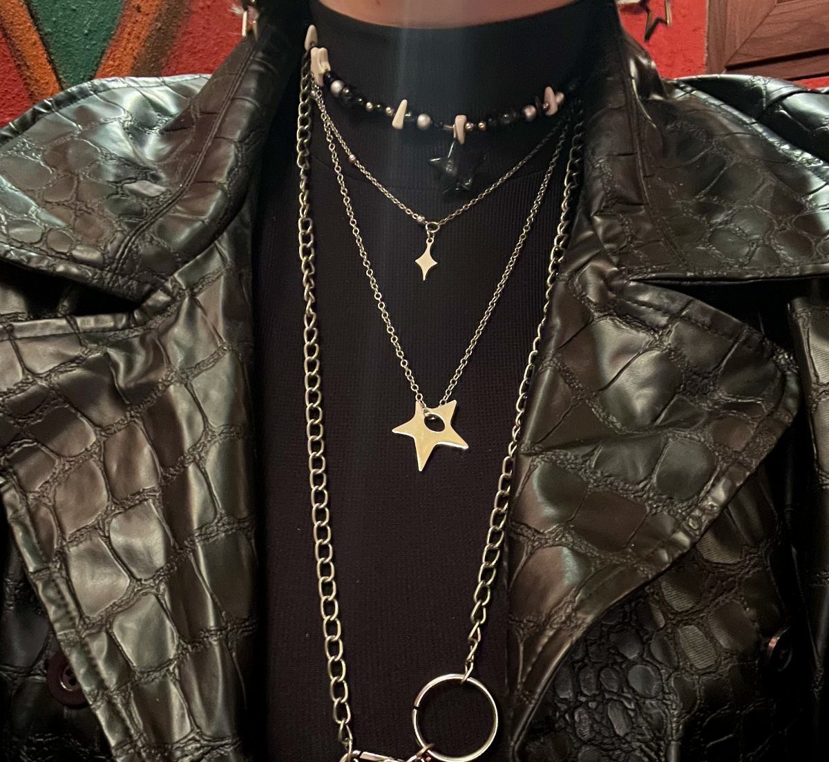 Multiple silver layered necklaces with star pendants worn over a black turtleneck and leather jacket.