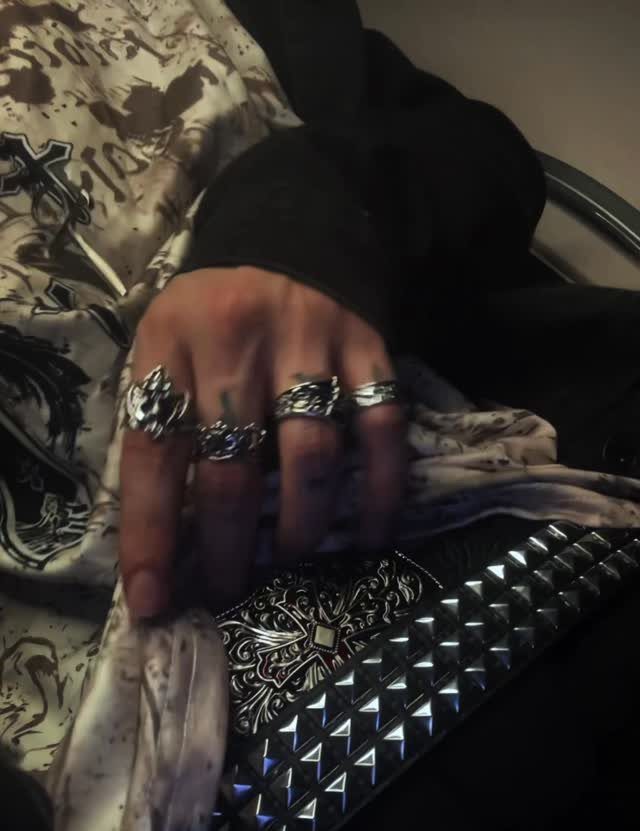 A hand adorned with multiple large silver rings resting near a black studded accessory.