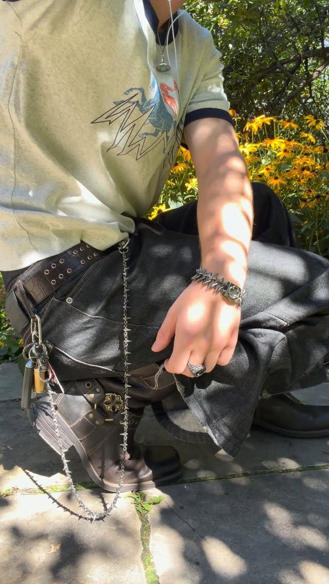 A person wearing studded belts, metal chains, a spiked bracelet, and a large silver ring.