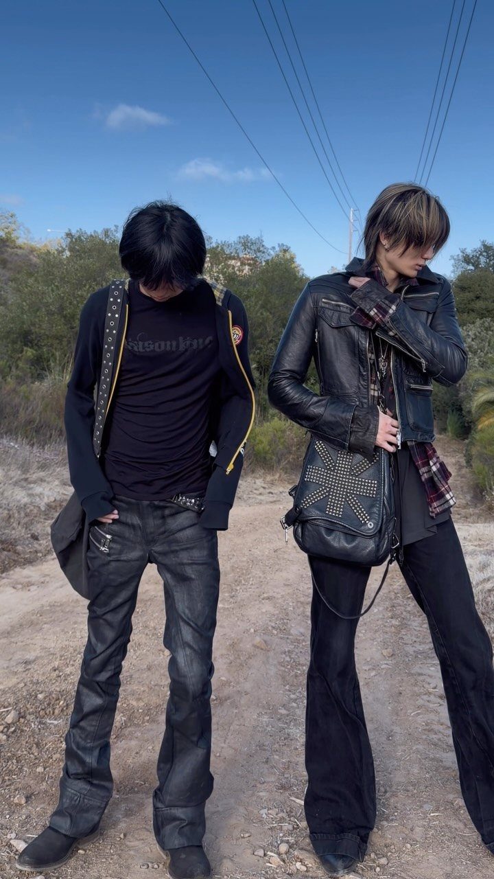 Two men dressed in dark gothic fashion standing on a dirt path outdoors.
