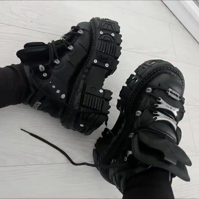 Black chunky platform combat boots with heavy lug soles and silver hardware on a light floor.