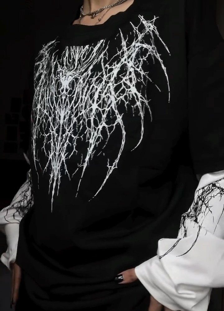 A person wearing a black shirt with a white thorny graphic design and a silver necklace.
