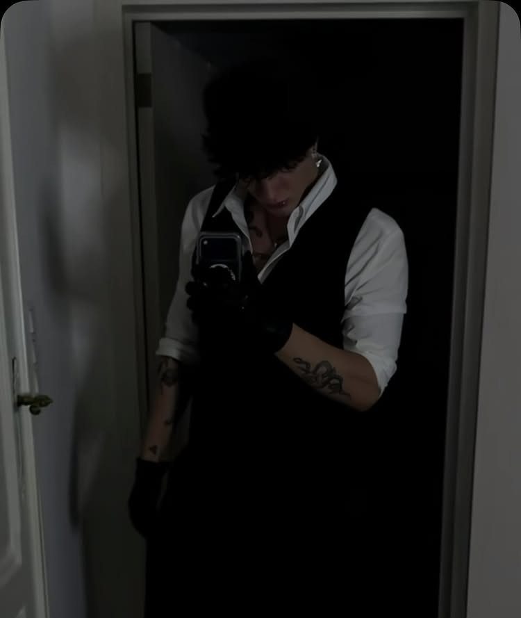 A man in a white shirt and black vest posing for a dark mirror selfie.