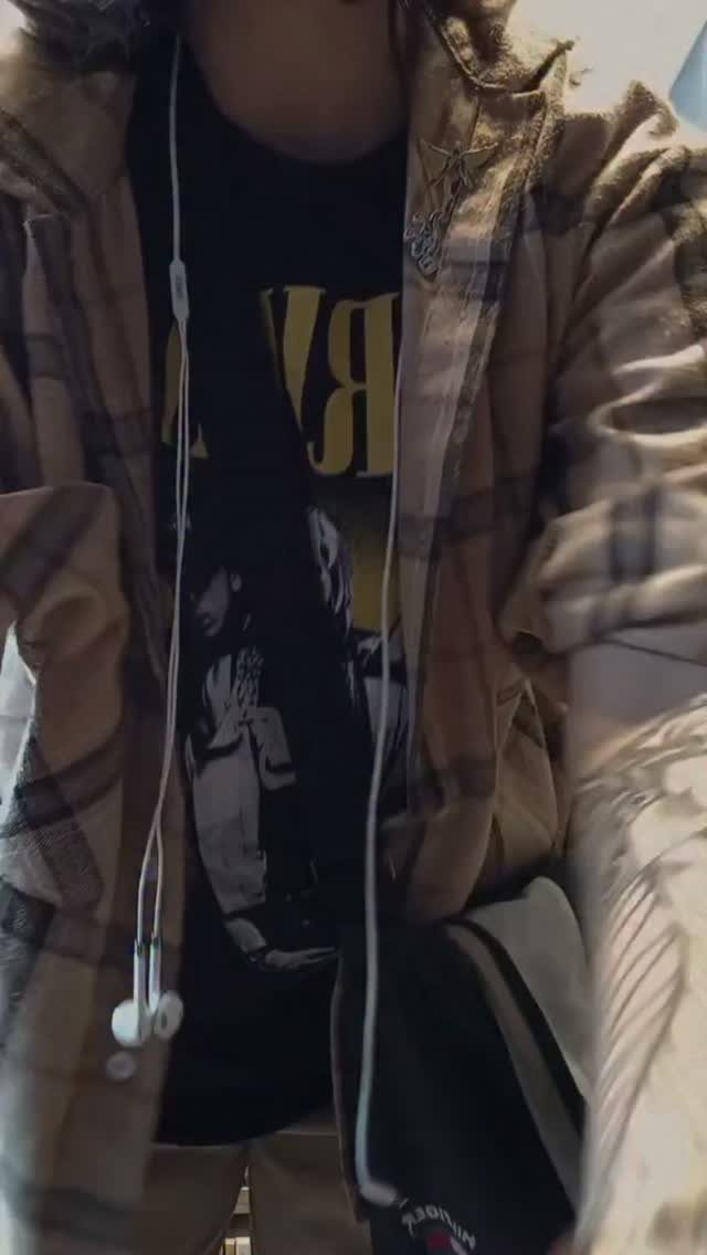 A person wearing a black graphic t-shirt and an open plaid flannel shirt with white earphones.