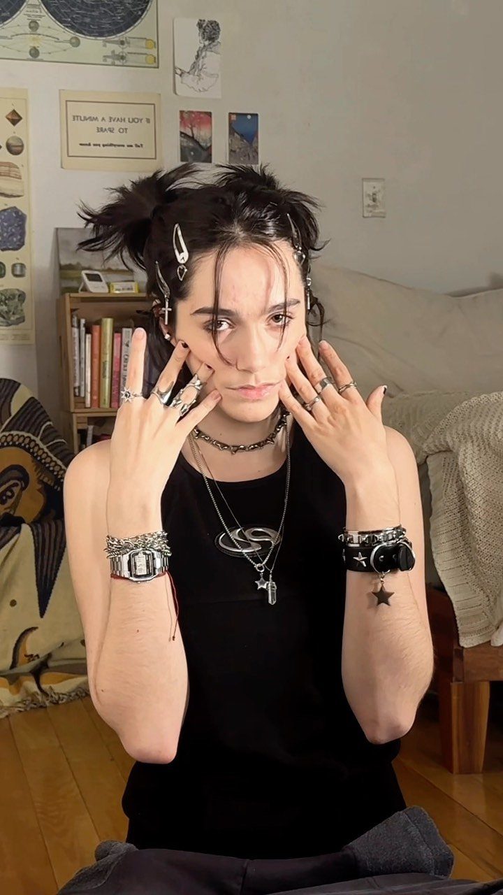 A person with dark hair styled in buns, adorned with silver hair clips and layered jewelry.