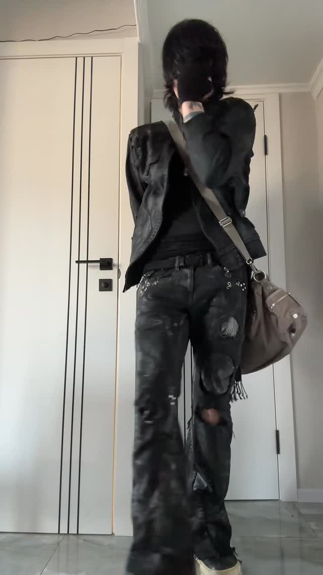 Person wearing a black jacket and black ripped jeans with a brown crossbody bag.