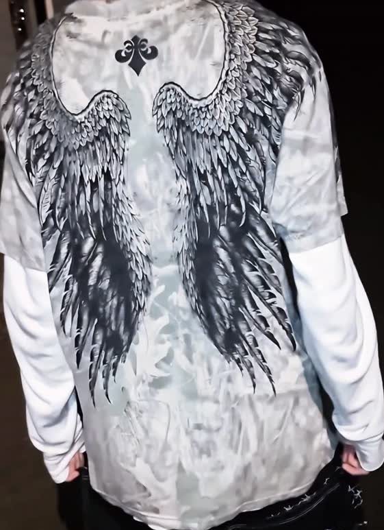 Person wearing a tie-dye t-shirt with large black and white angel wings printed on the back.