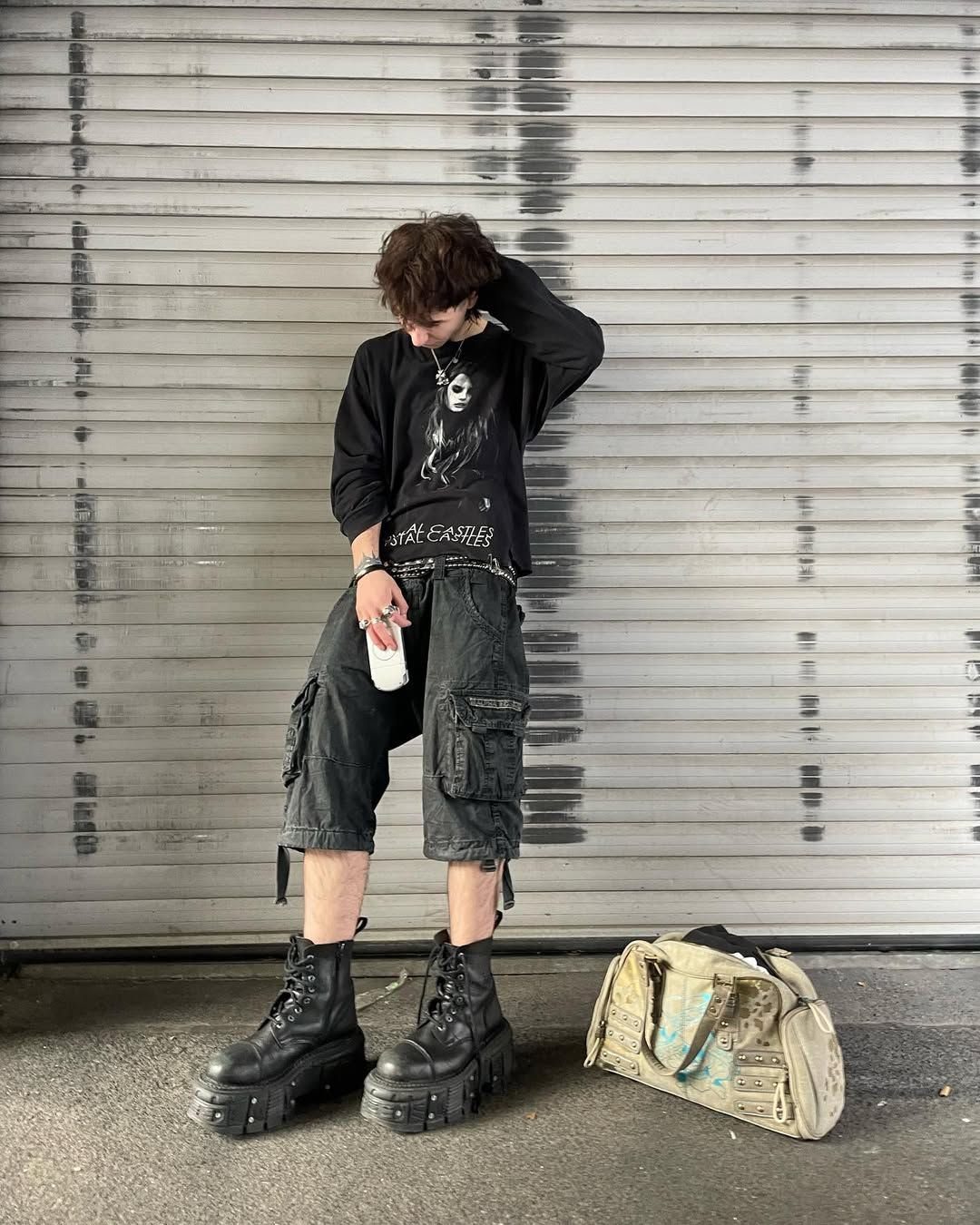 A person wearing black graphic shirt, cargo shorts, and large black chunky platform boots.