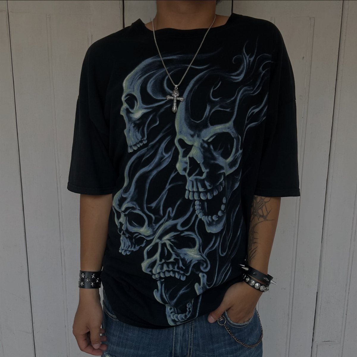 A person wearing a black t-shirt with large blue skull graphics and a silver cross necklace.