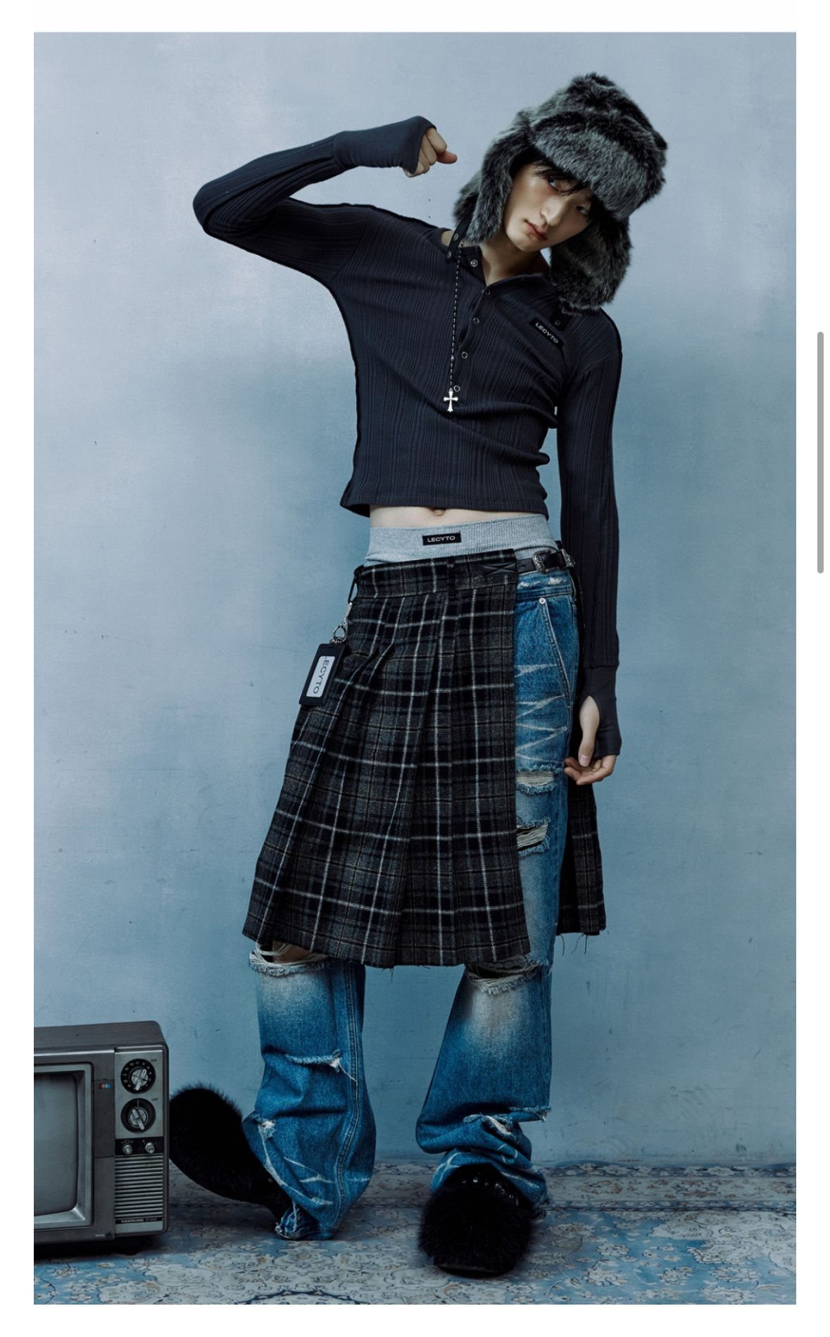 Person wearing a black long-sleeve top, plaid pleated skirt, and distressed denim jeans.