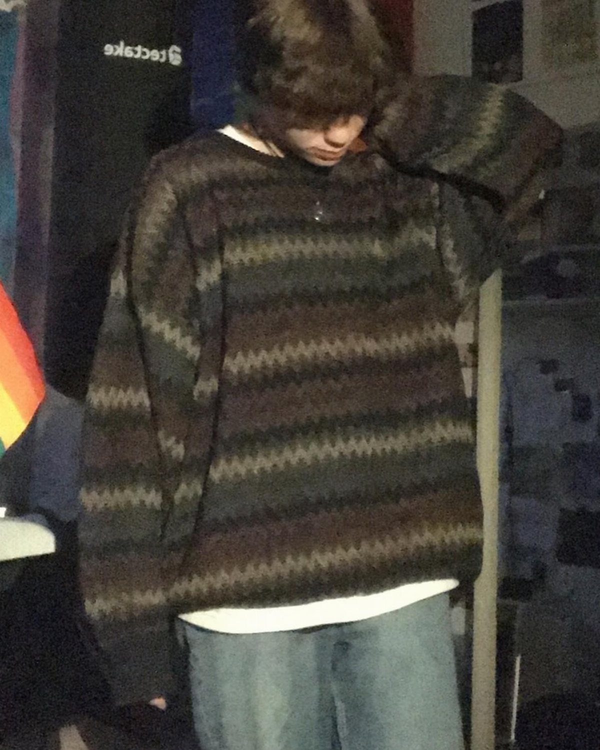 A person wearing a dark patterned oversized zigzag sweater and light blue jeans.