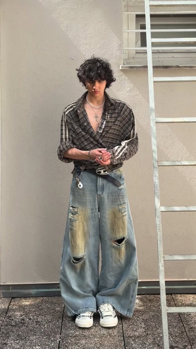 A person wearing a plaid shirt and oversized distressed wide-leg denim jeans standing outdoors.