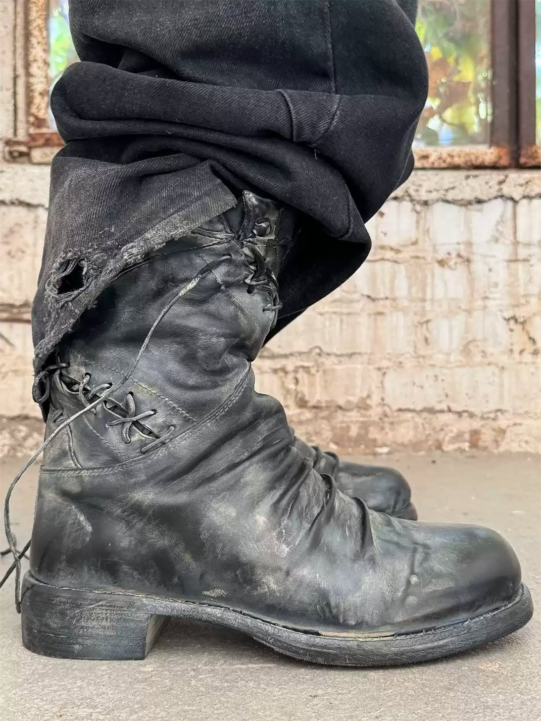 Distressed black leather lace-up boots worn with ripped black denim jeans.